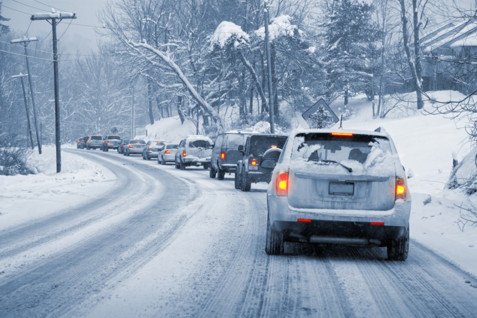 Line of cars driving slowly on a snowy road.