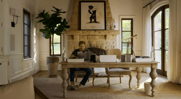 a man sits at a desk in front of a fireplace using a laptop