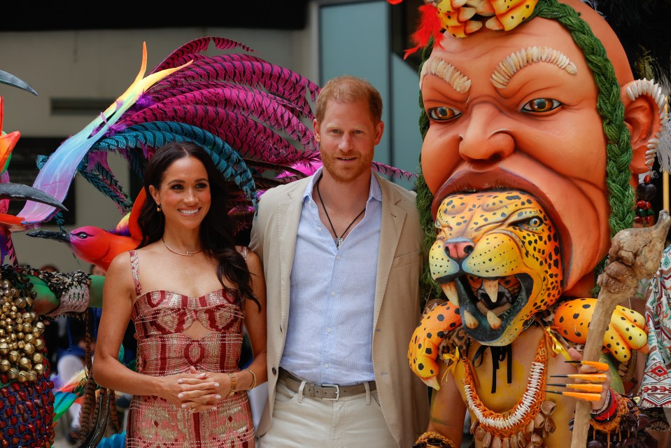 prince harry and meghan markle pose in front of a colorful statue