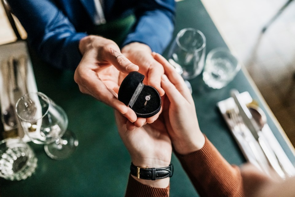 A man proposing to his girlfriend with an engagement ring in a restaurant.