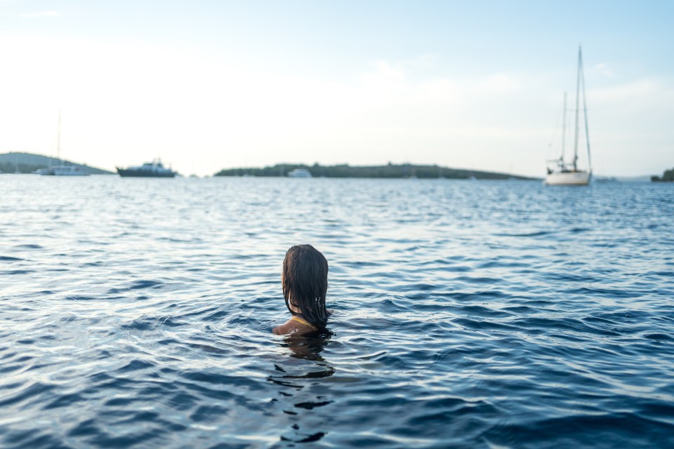 a woman is swimming in the ocean with boats in the background