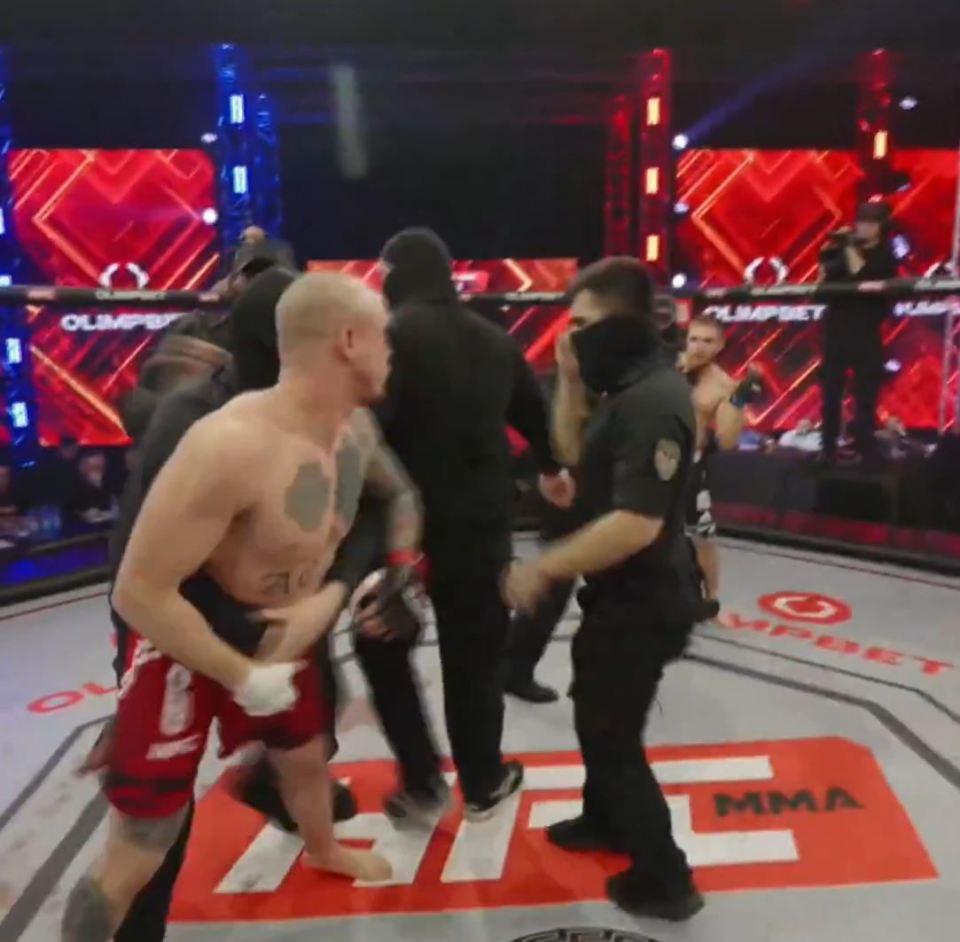 A fighter being escorted out of an MMA cage.