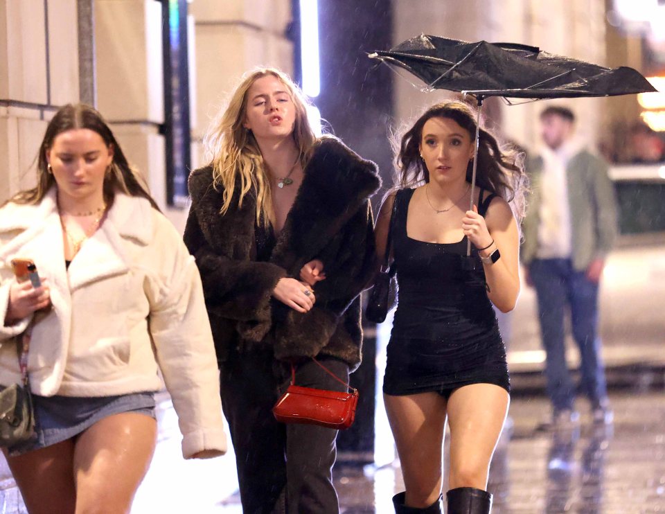Three young women walking in the rain on New Year's Eve. One woman holds an umbrella.