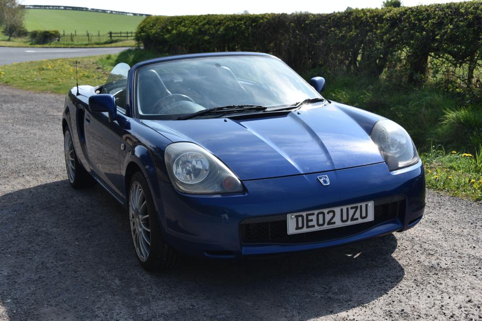 Blue Toyota MR2 convertible parked on a road.