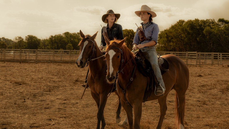 Two women on horseback in a field.