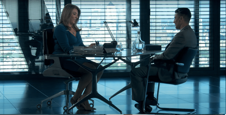 A woman and a man sitting across a glass table in a modern office.