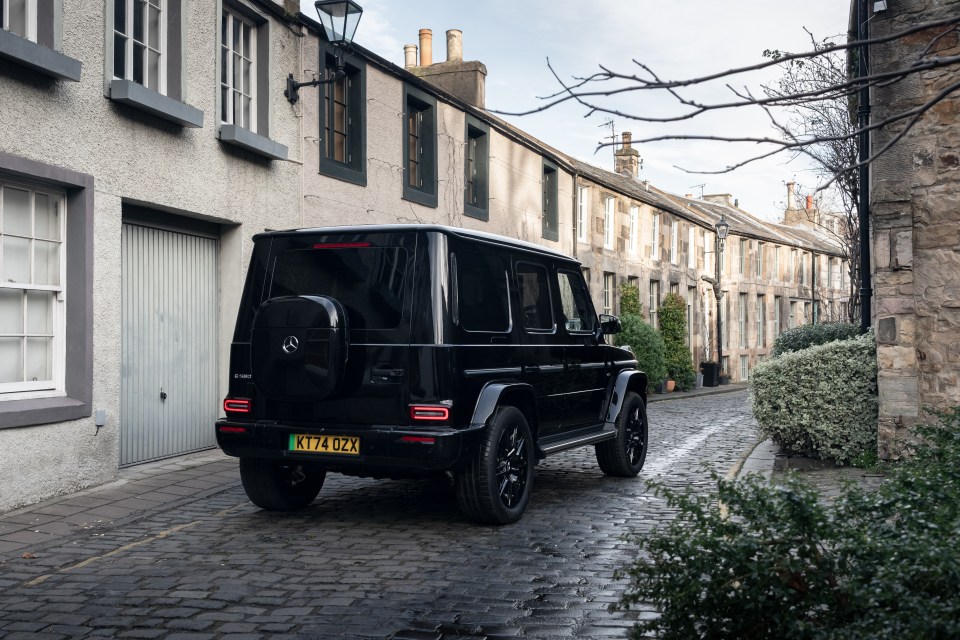 Black Mercedes G-Class driving down a cobblestone street.