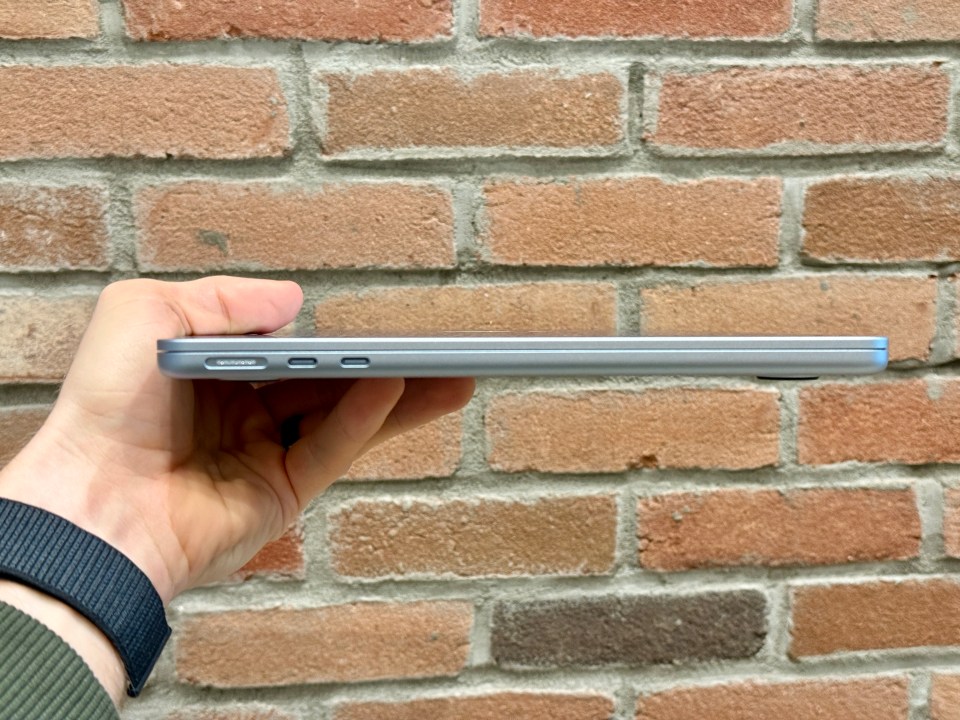 Side profile of a silver laptop held in a hand against a brick wall.