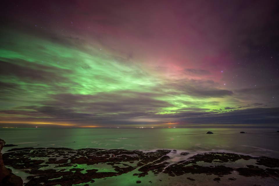 Aurora borealis over a calm sea and rocky shore.