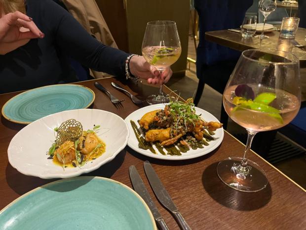 Two plates of food and two cocktails on a restaurant table.