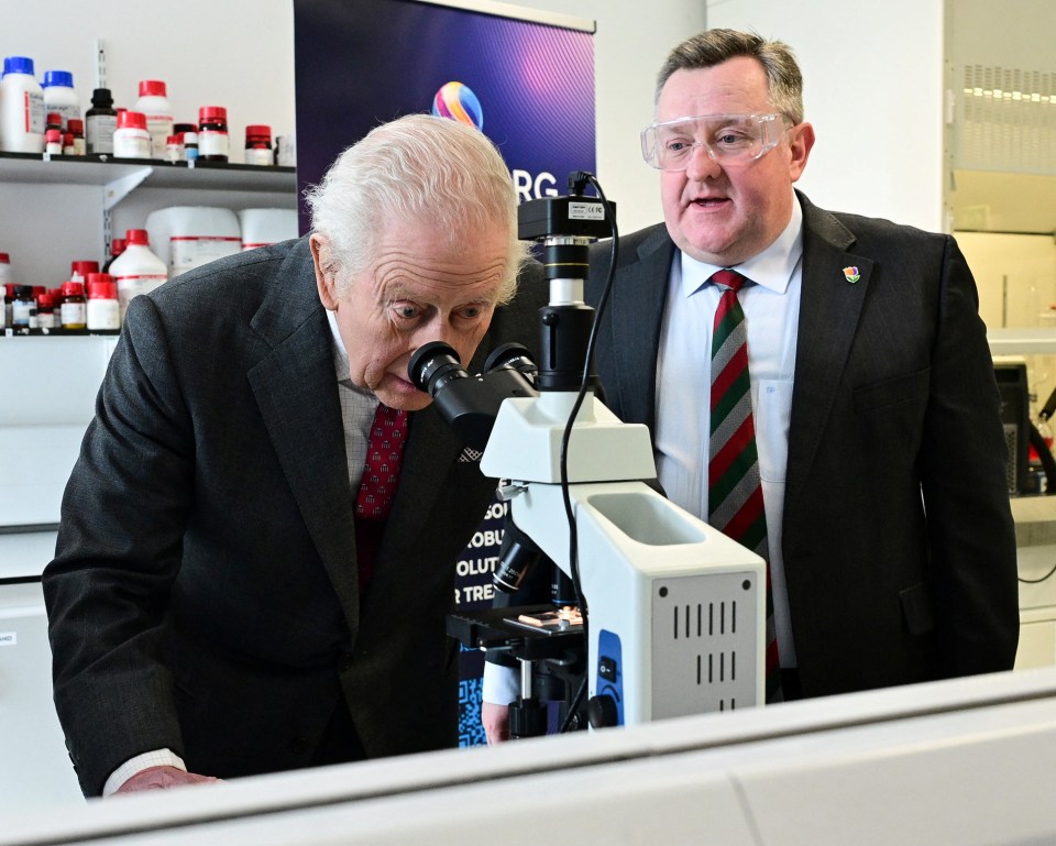 King Charles III looking through a microscope in a lab.