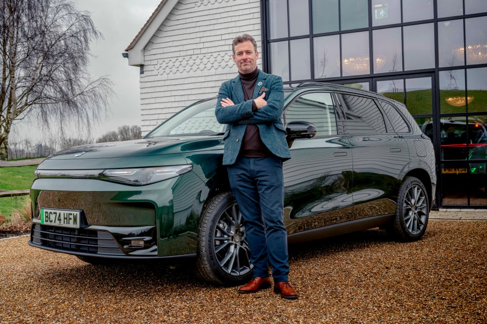 Man standing with arms crossed next to a dark green SUV.