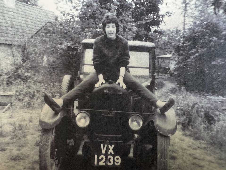 Black and white photo of a young woman sitting on a vintage car.
