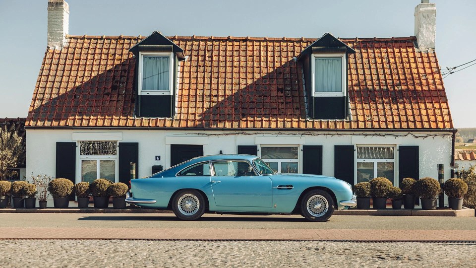 Light blue Aston Martin DB5 parked in front of a house.