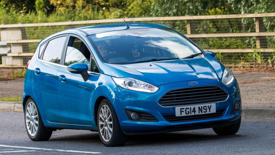 Blue Ford Fiesta driving on a road.