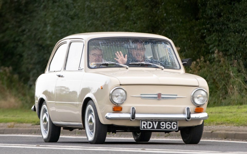 A beige 1969 Fiat 850 driving down a country road.