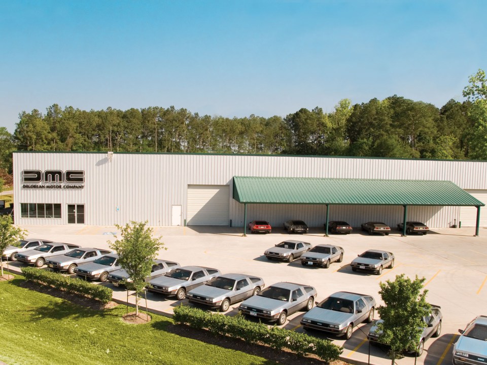 DeLorean Motor Company building with numerous DeLorean cars parked in front.