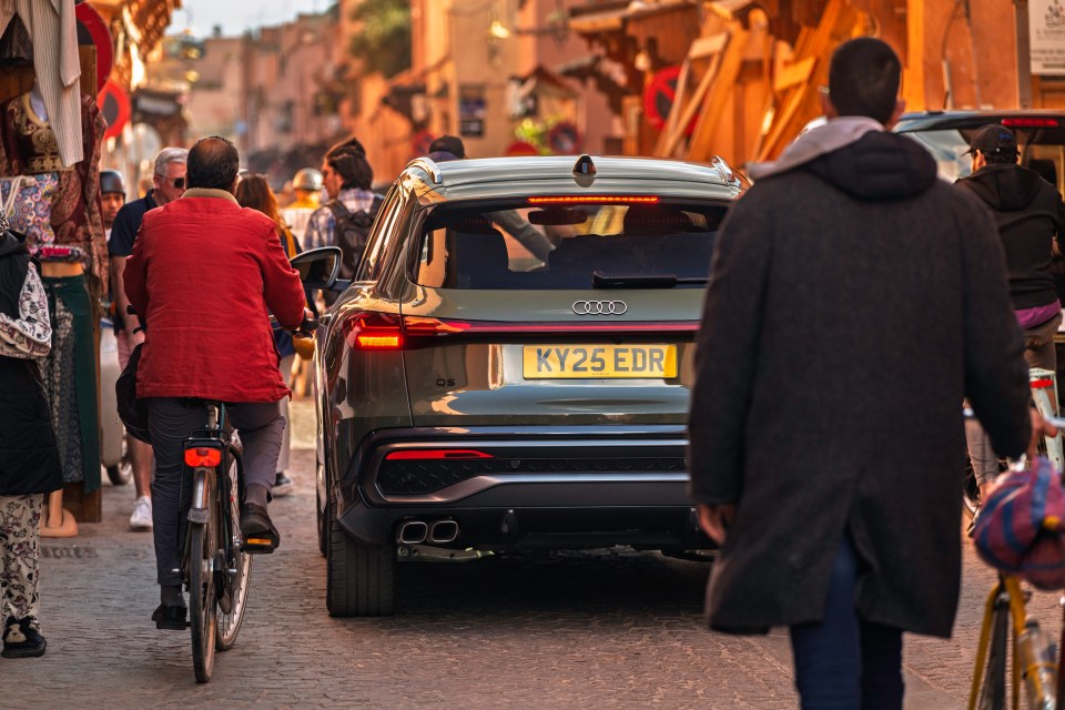 Rear view of a green Audi Q5 driving down a narrow street.