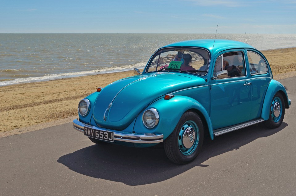 Teal Volkswagen Beetle driving along a beach.
