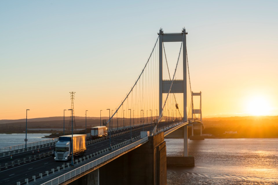 A truck crossing a suspension bridge at sunset.