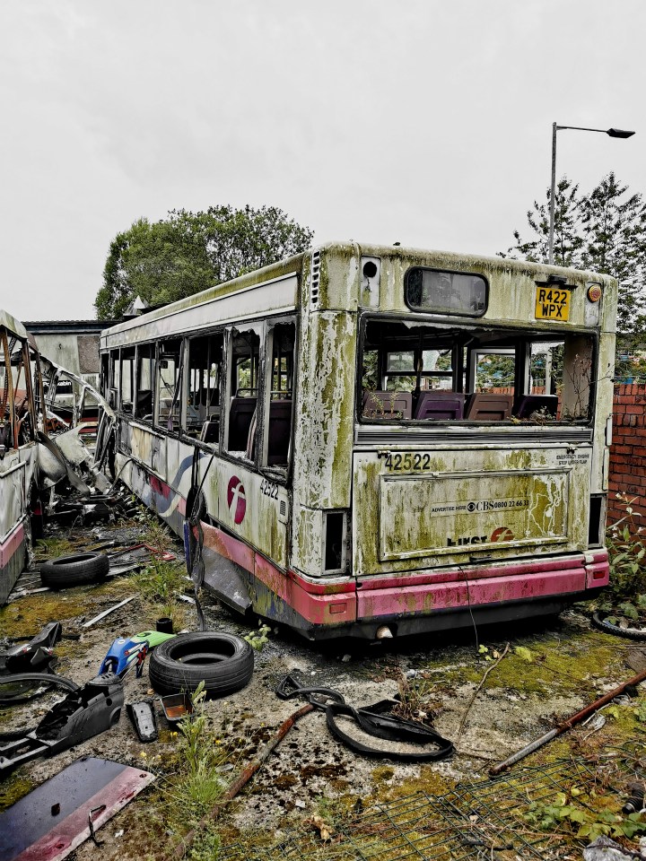 A dilapidated bus in a graveyard of abandoned vehicles.