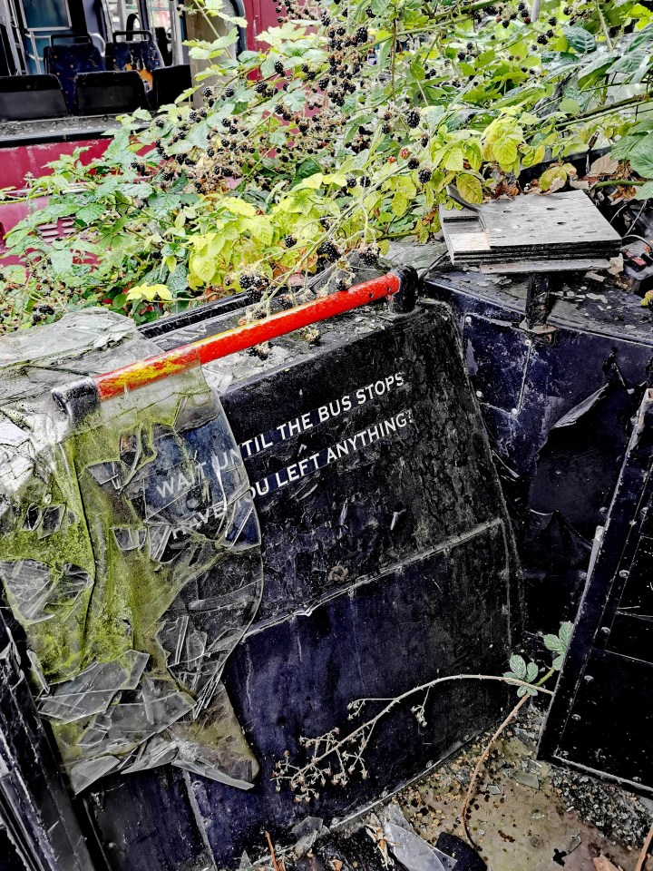Close-up of a wrecked bus interior with broken glass and the message "Wait until the bus stops" visible.