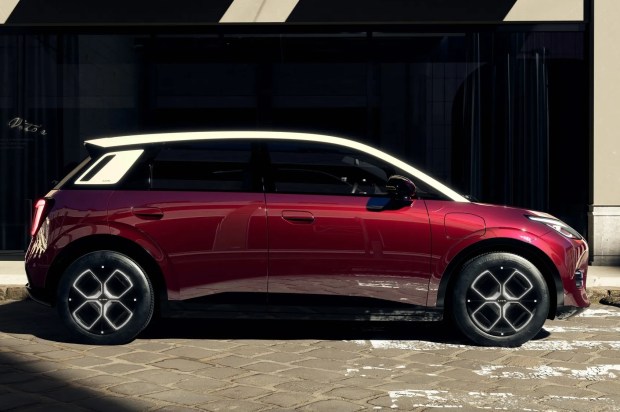 Red Aion electric car parked on cobblestones.