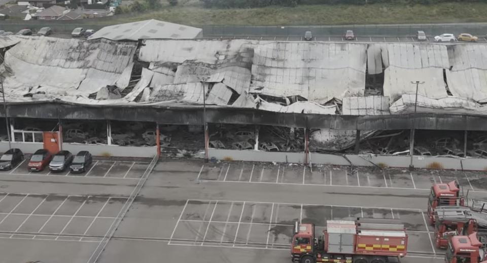 Aerial view of a fire-damaged building with collapsed roof and burned cars inside.