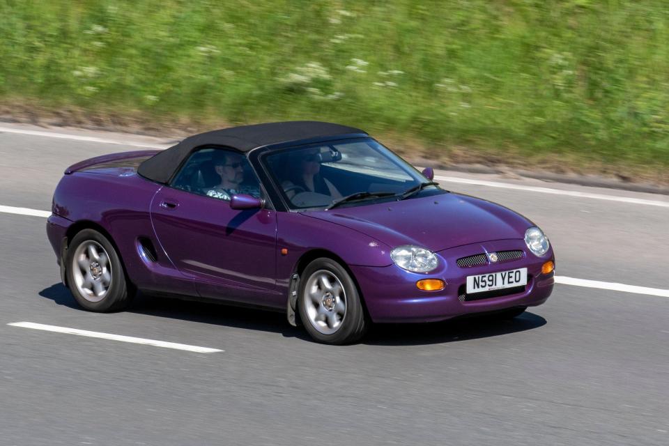 Purple MG F convertible driving on a highway.