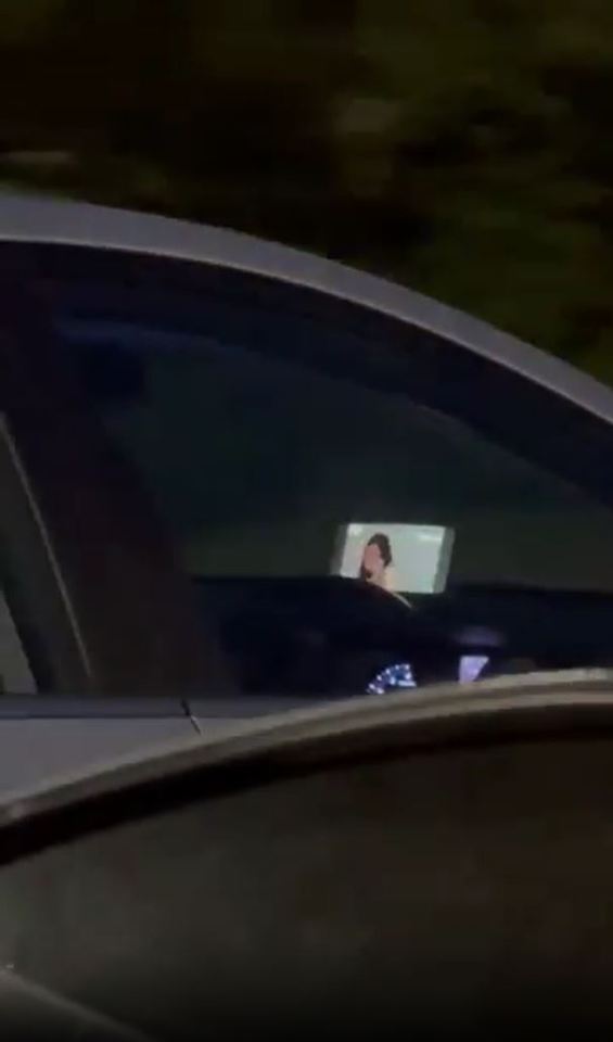 Person reflected in car window watching video on screen.