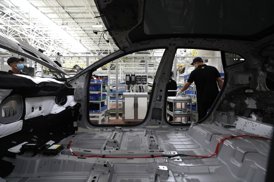 Workers assembling an electric SUV on a factory assembly line.