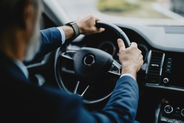 Close-up image of a businessman driving a car, emphasizing the driver's hands on the steering wheel and wearing a suit.