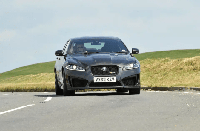 Dark gray Jaguar XJR driving on a road.
