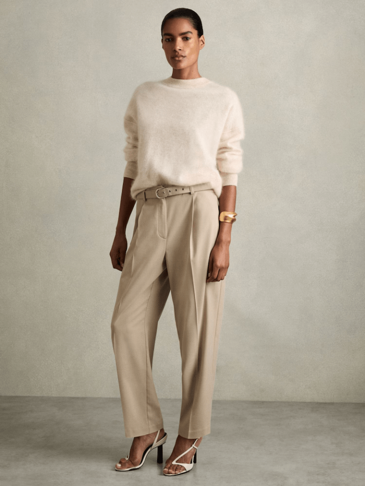 Woman wearing a cream sweater, beige trousers, and white heels.