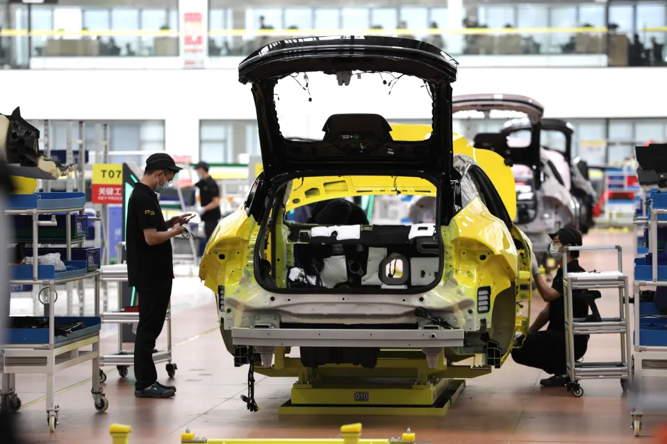 Car assembly line workers constructing a yellow car.