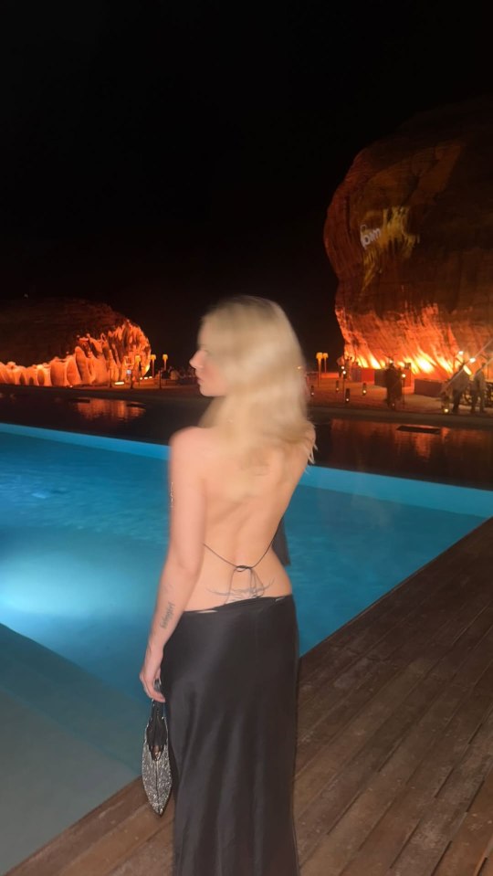 Woman in backless black dress by a pool at night.