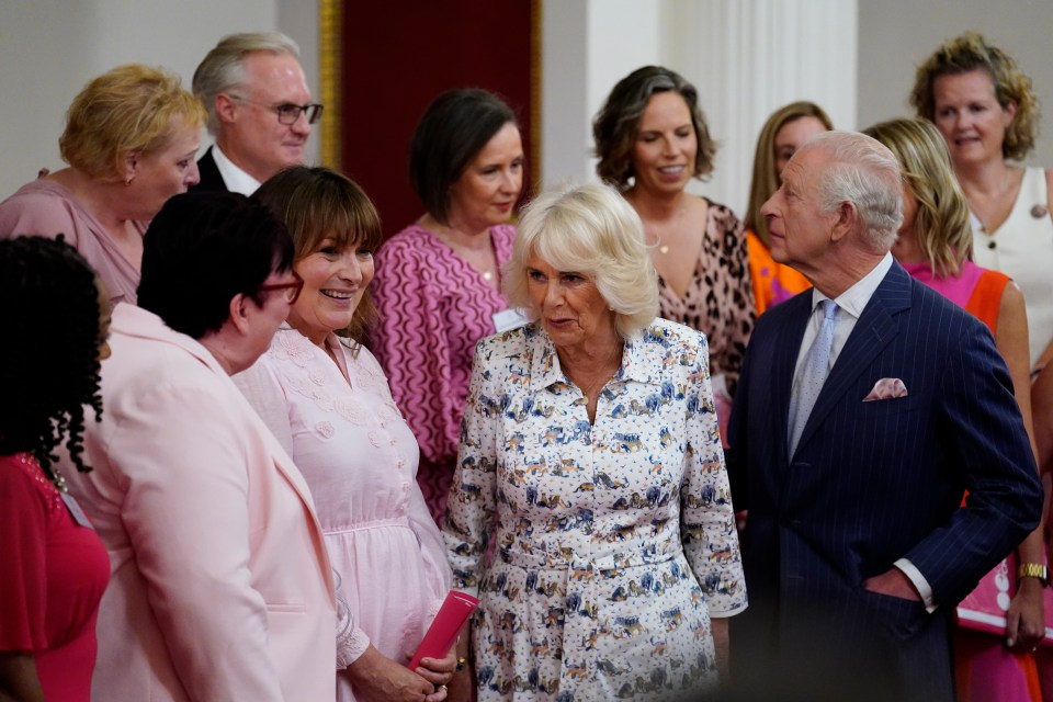 King Charles III and Queen Camilla speaking with guests at a Buckingham Palace reception.