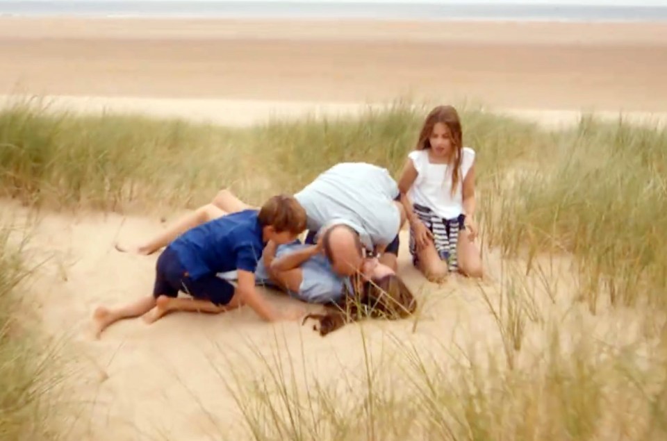 Family on a beach; parents kissing while children play nearby.