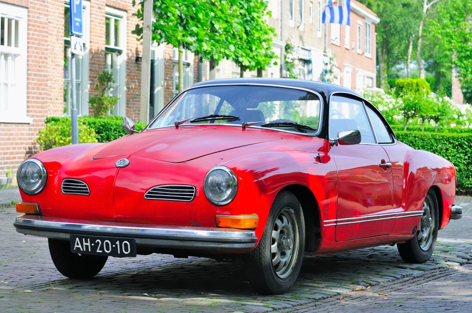 Red classic Volkswagen Karmann Ghia parked on a cobblestone street.