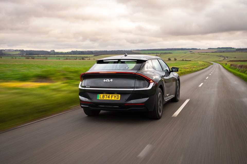 Rear view of a dark gray Kia EV6 driving on a country road.