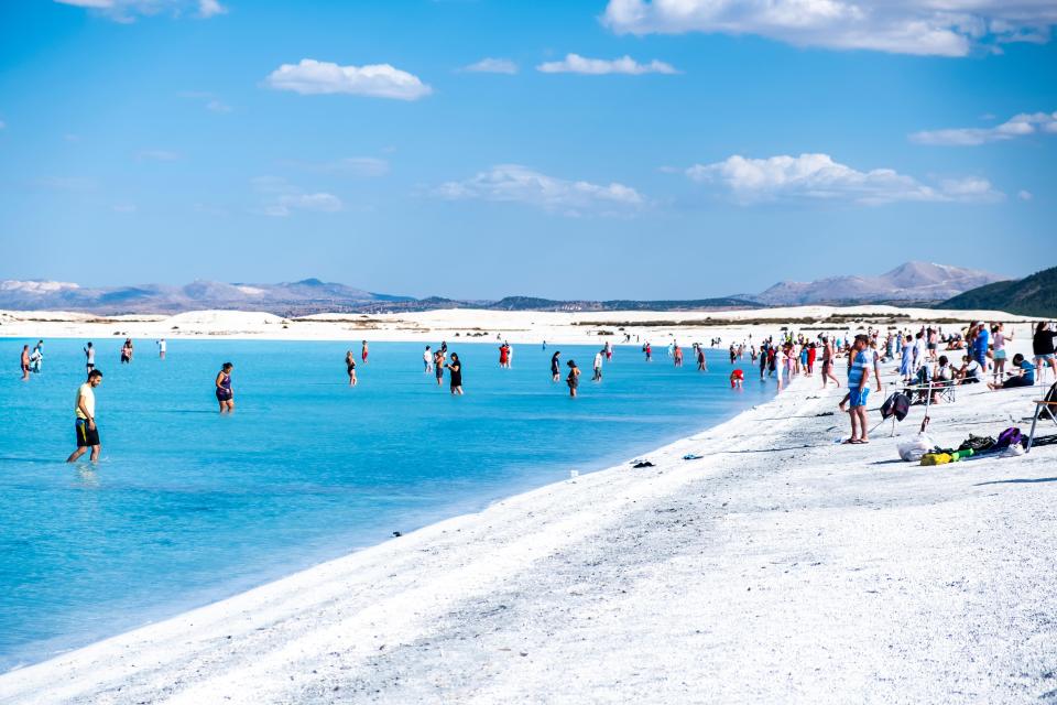 People swimming and relaxing on the white sand beach of Lake Salda, Turkey.