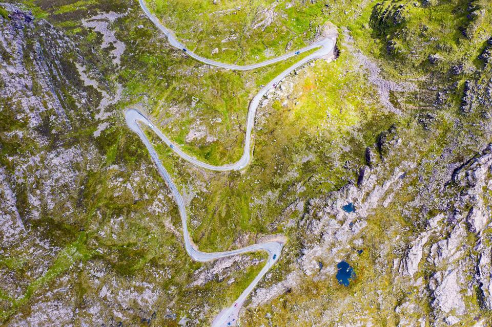 Aerial view of Bealach na Ba pass with cars driving on a winding road.
