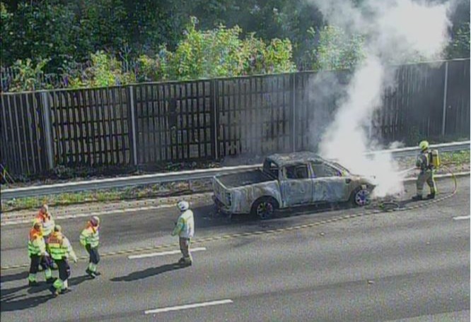 Burning pickup truck on highway with firefighters.