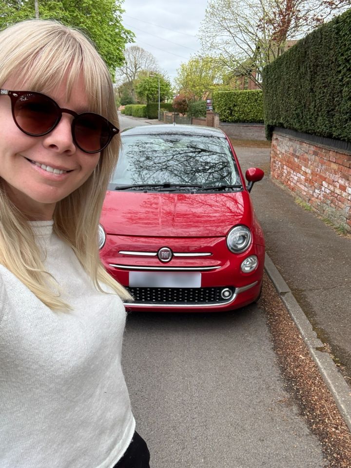 Woman in sunglasses standing next to a red Fiat 500.
