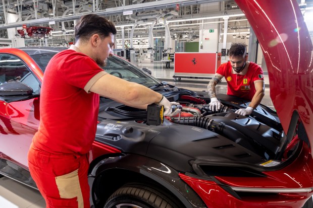 Two workers in red Ferrari shirts working on a red Ferrari's engine.