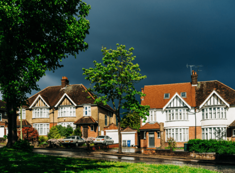 Two houses on a residential street under a dark sky.