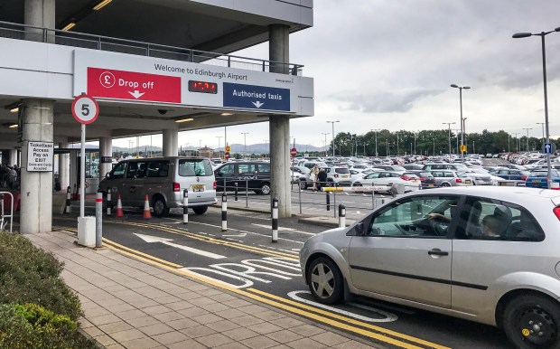 Edinburgh Airport drop-off zone with cars and signage.