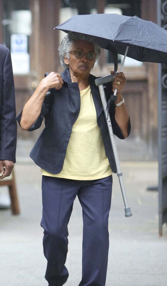 Woman with cane and umbrella outside courthouse.