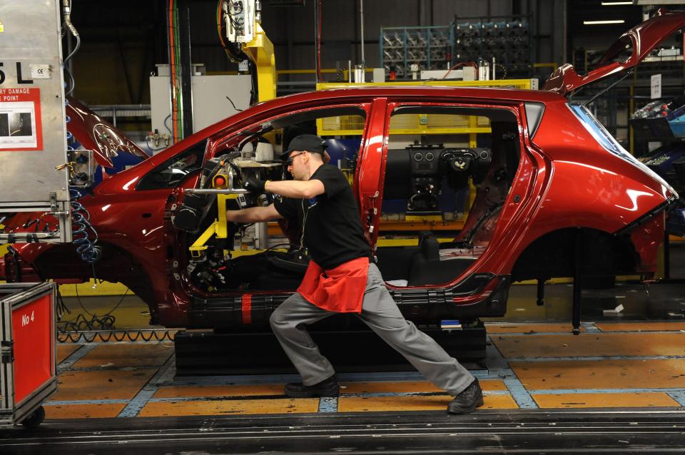 Worker installing a dashboard in a red Nissan Leaf on a car production line.