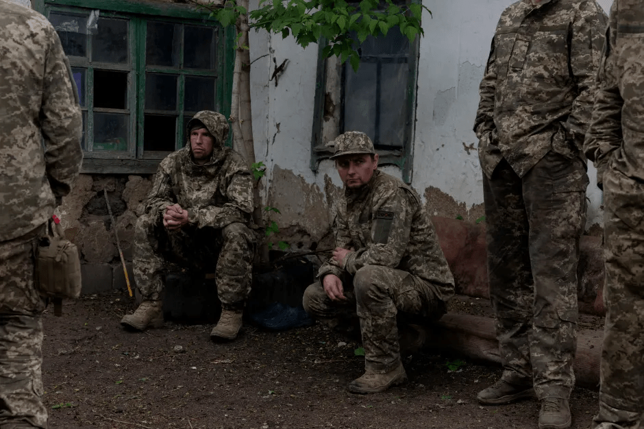 Soldiers in camouflage resting near a building.